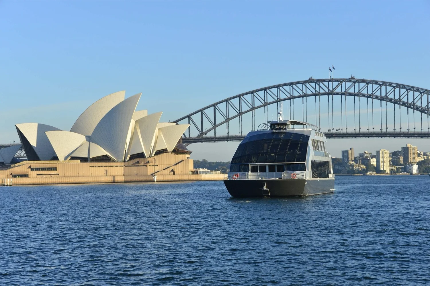 Clearview, a glass-walled event boat, cruising Sydney Harbour on a sunny day beside the Opera House and Harbour Bridge