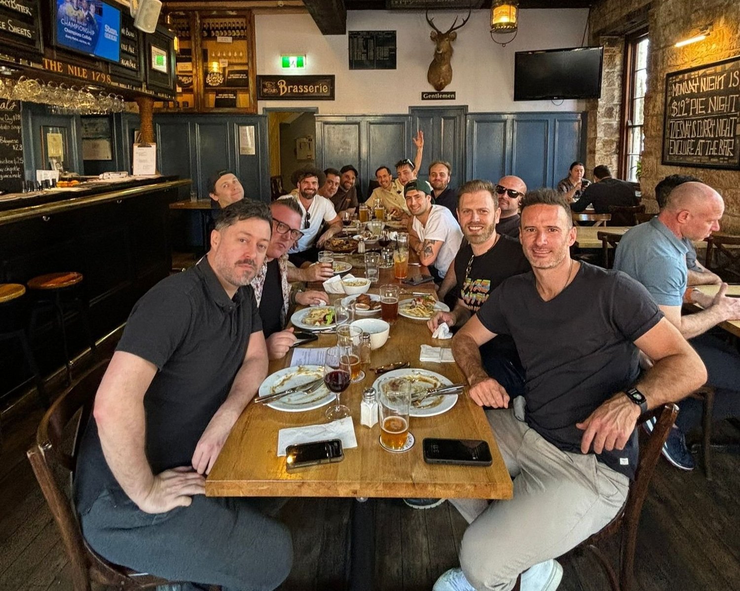 A bucks party group seated along a timber table with beers and meals in a Hunter Valley brewery restaurant, part way through a brewery tour with go karting.