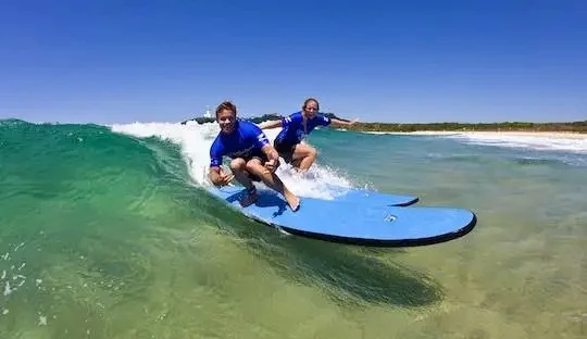 Two people riding a small wave during a beginner surf lesson at Byron Bay