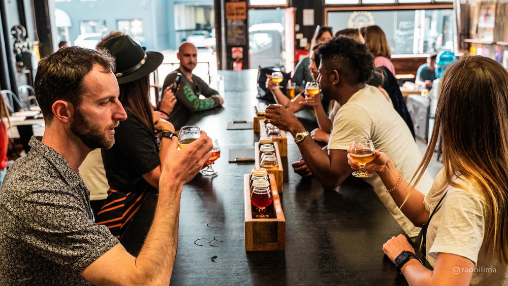 Guests sitting along a taproom bar with tasting paddles and half-finished glasses of beer in front of them