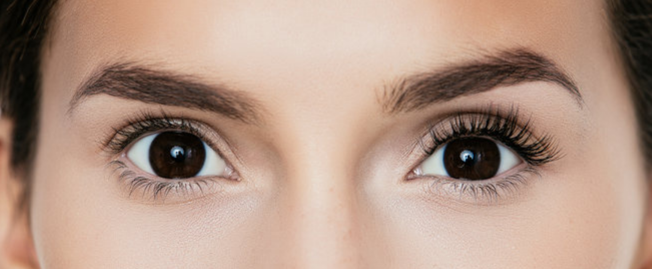 Close-up of a woman’s face showing her bare eyelashes on the left and classic full set extensions on the right.