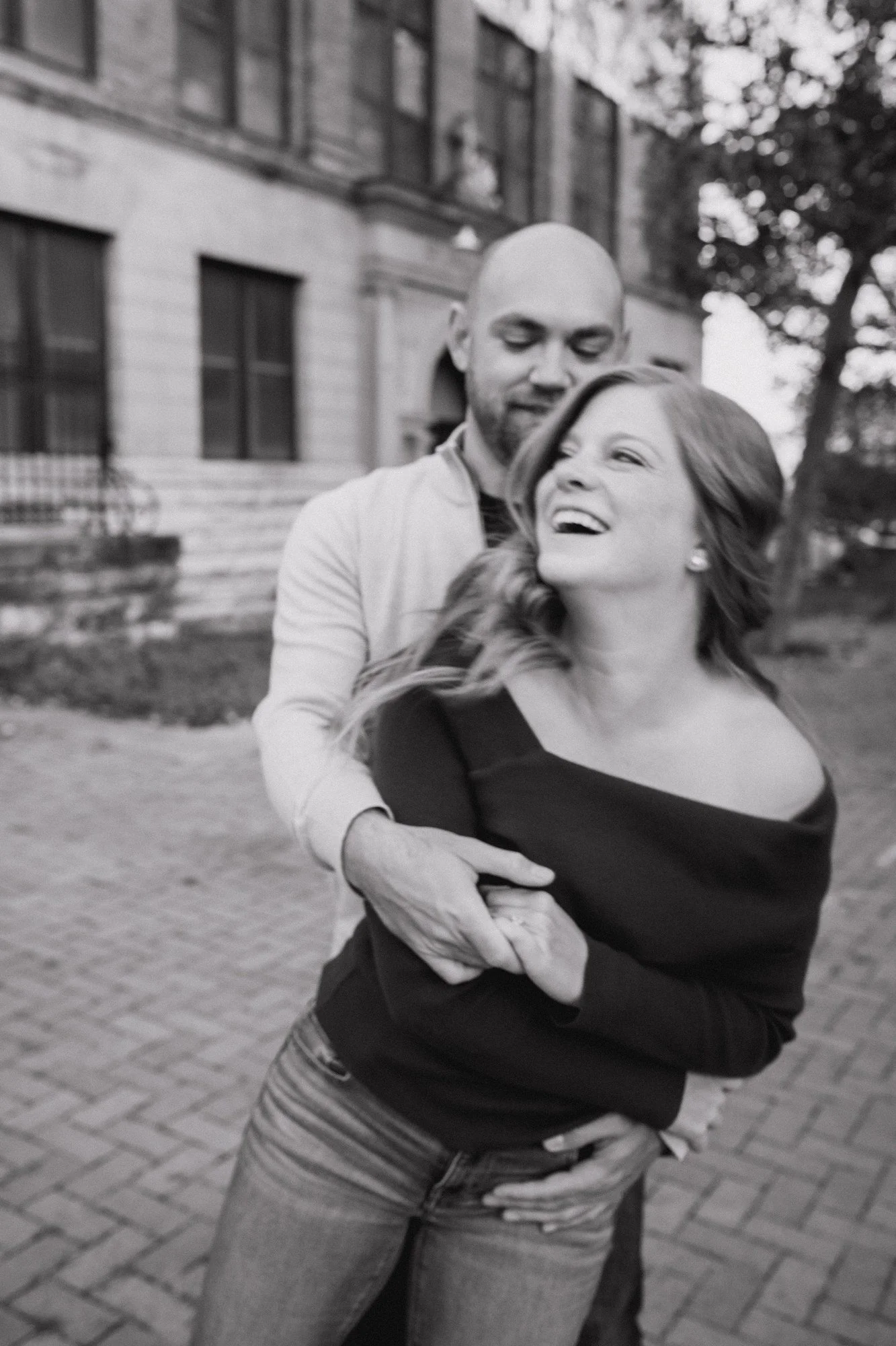 Black-and-white photograph of Erin laughing as Jacob embraces her from behind.