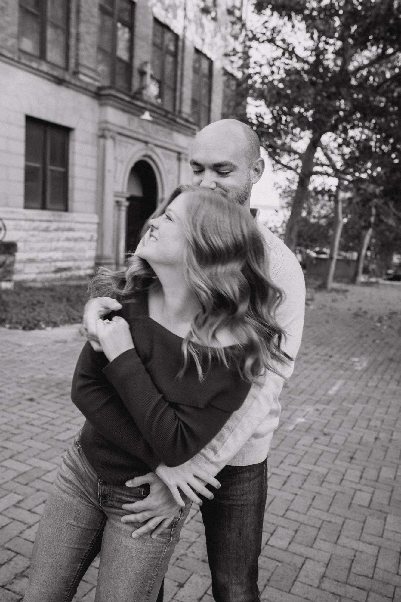 Black-and-white photograph of Jacob holding Erin close on a brick sidewalk.