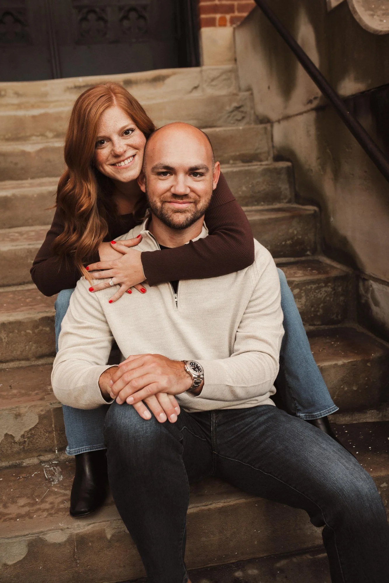 Erin wrapping her arms around Jacob while seated behind him on stone steps.