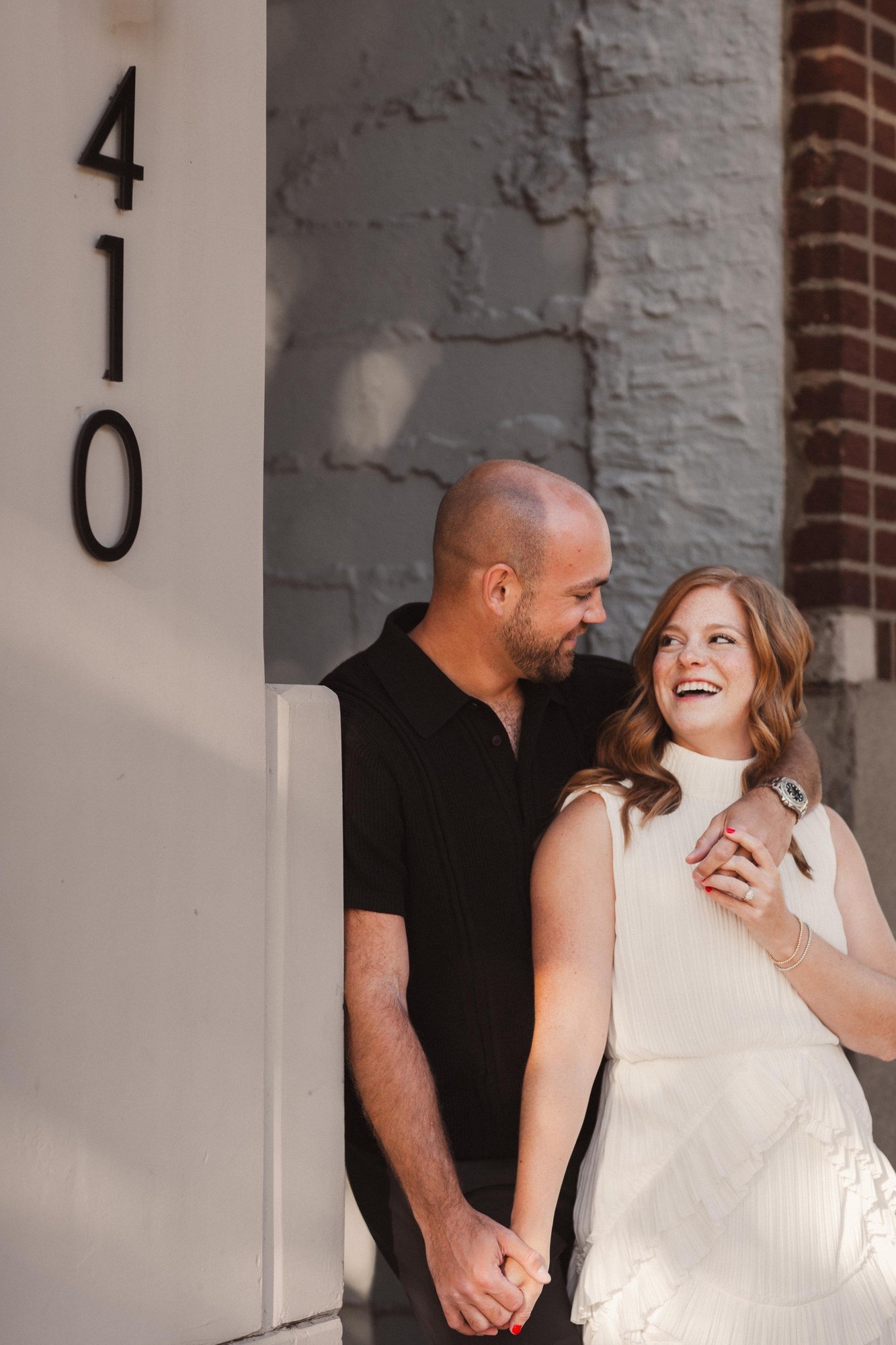 Erin laughing beside Jacob against a pale stone wall.