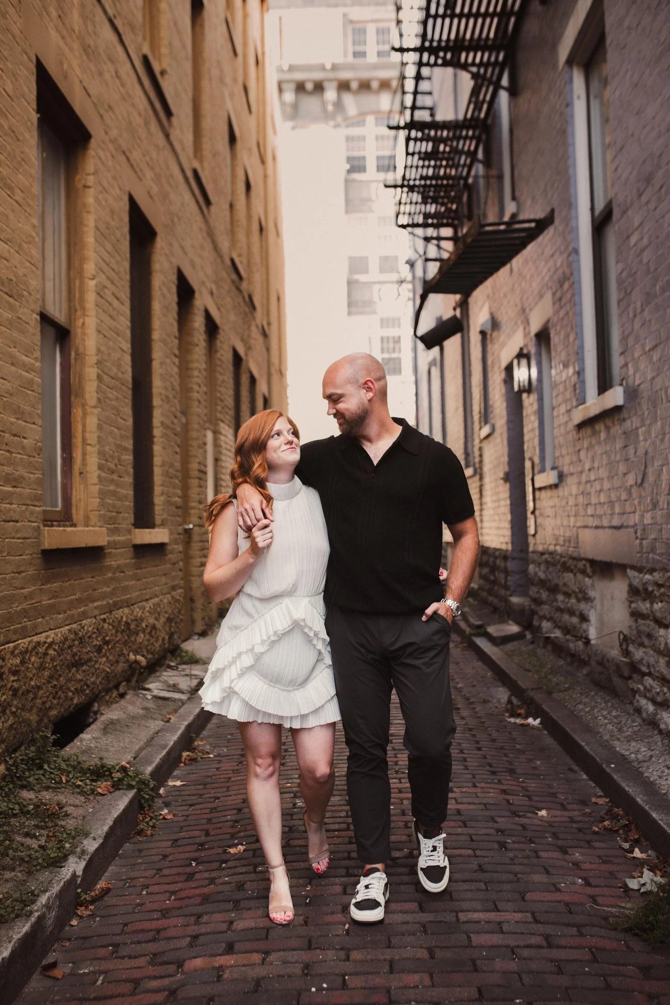 Erin looking toward Jacob as they walk together along a brick alley.