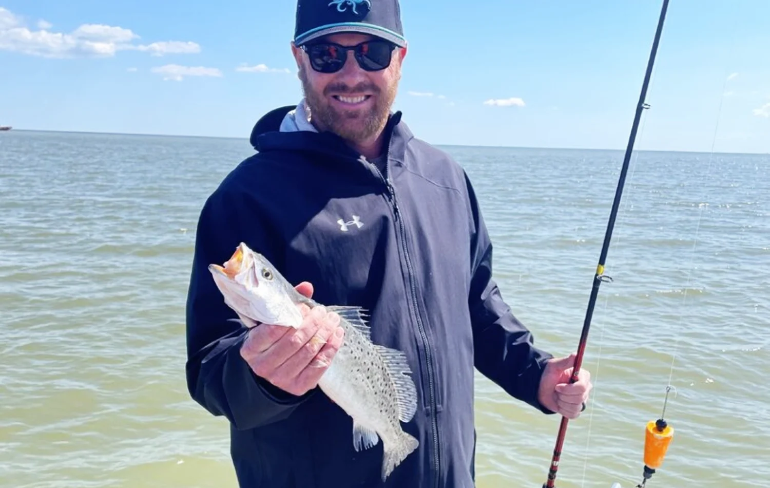 Texas Crew'd angler holding a speckled trout with a fishing rod