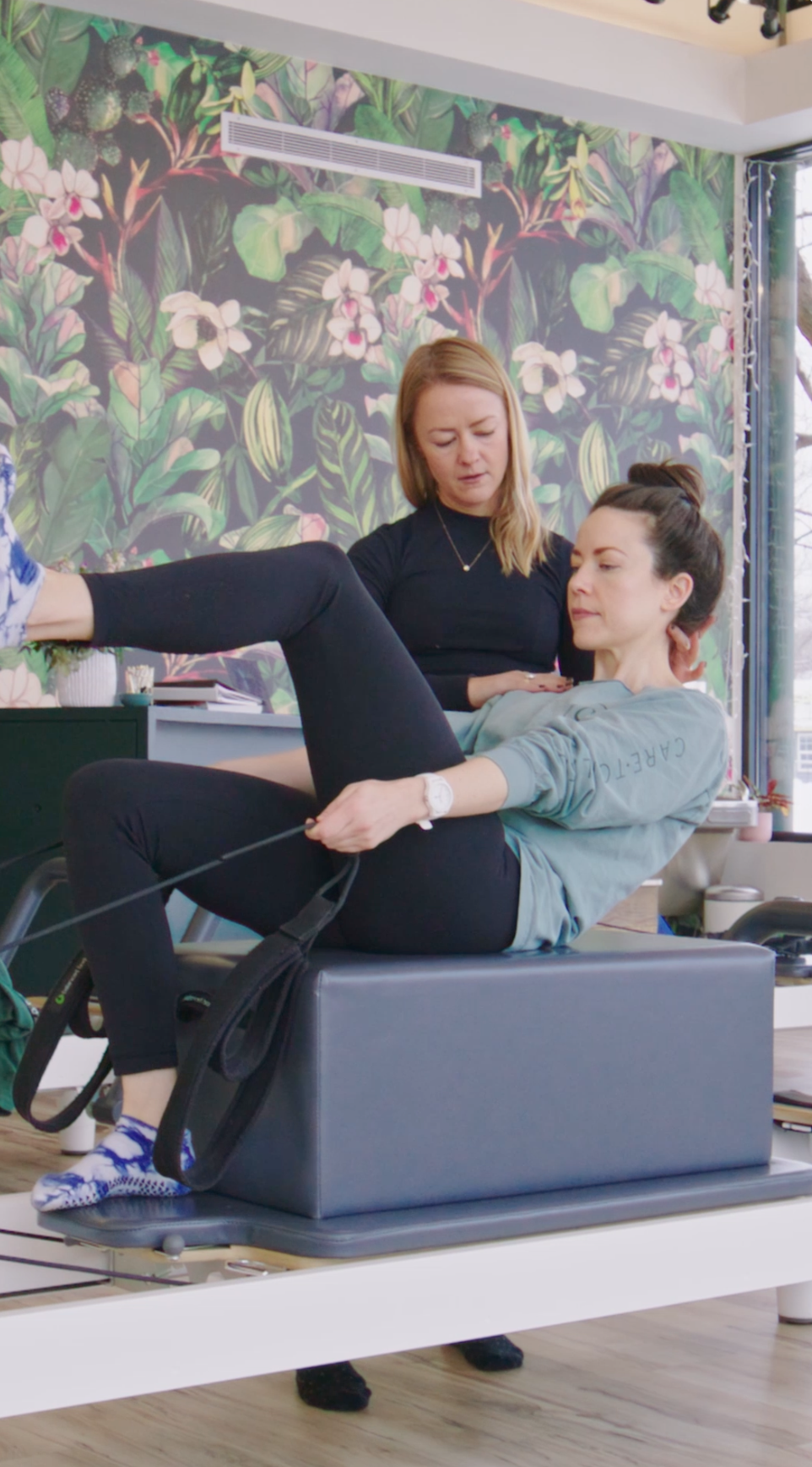 An instructor guiding a student through a reformer exercise at Care·To
