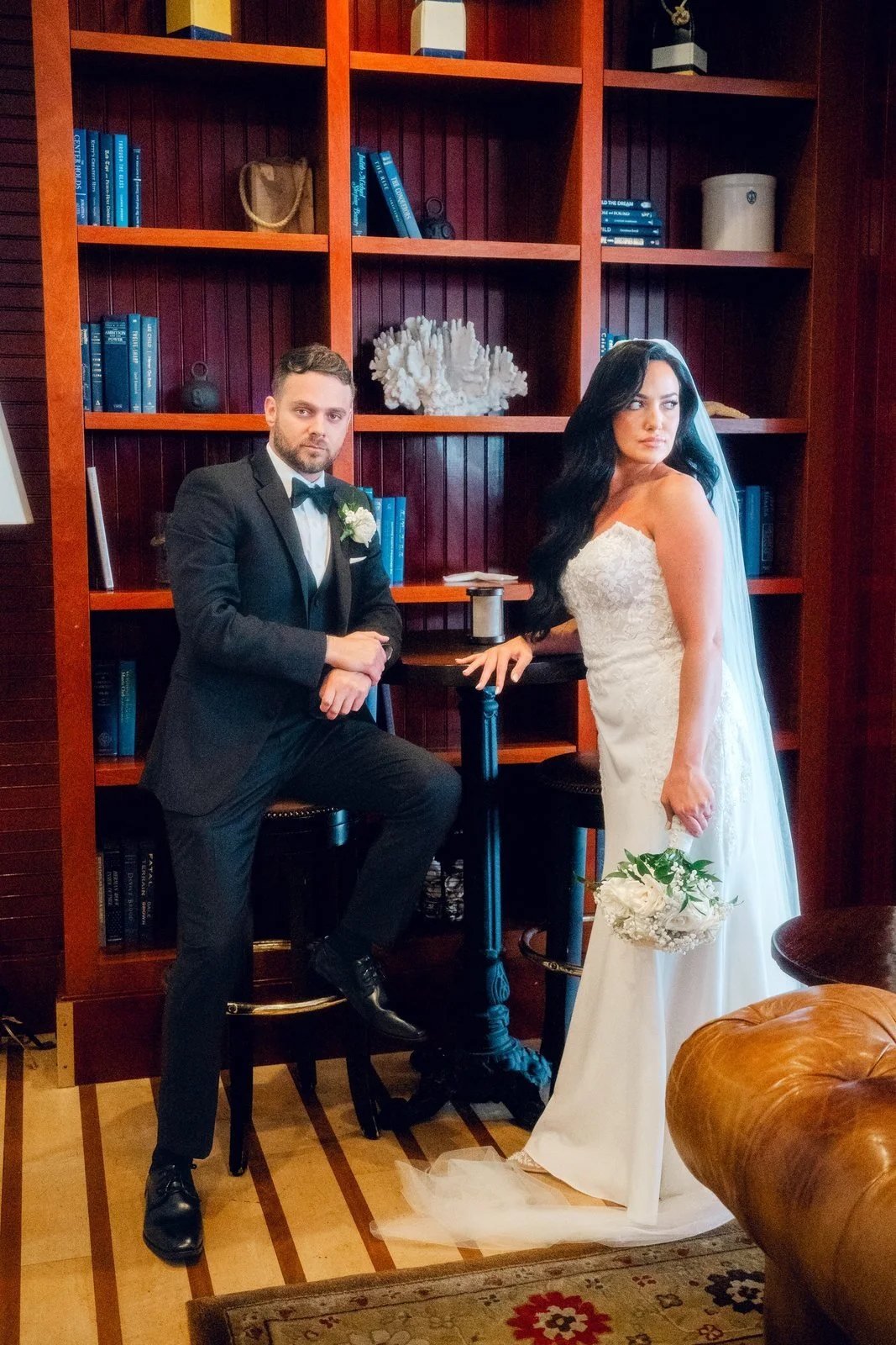 Beauport Hotel wedding videographer, Gloucester, MA — bride and groom sharing a laugh beside red bookshelves in a hotel lounge