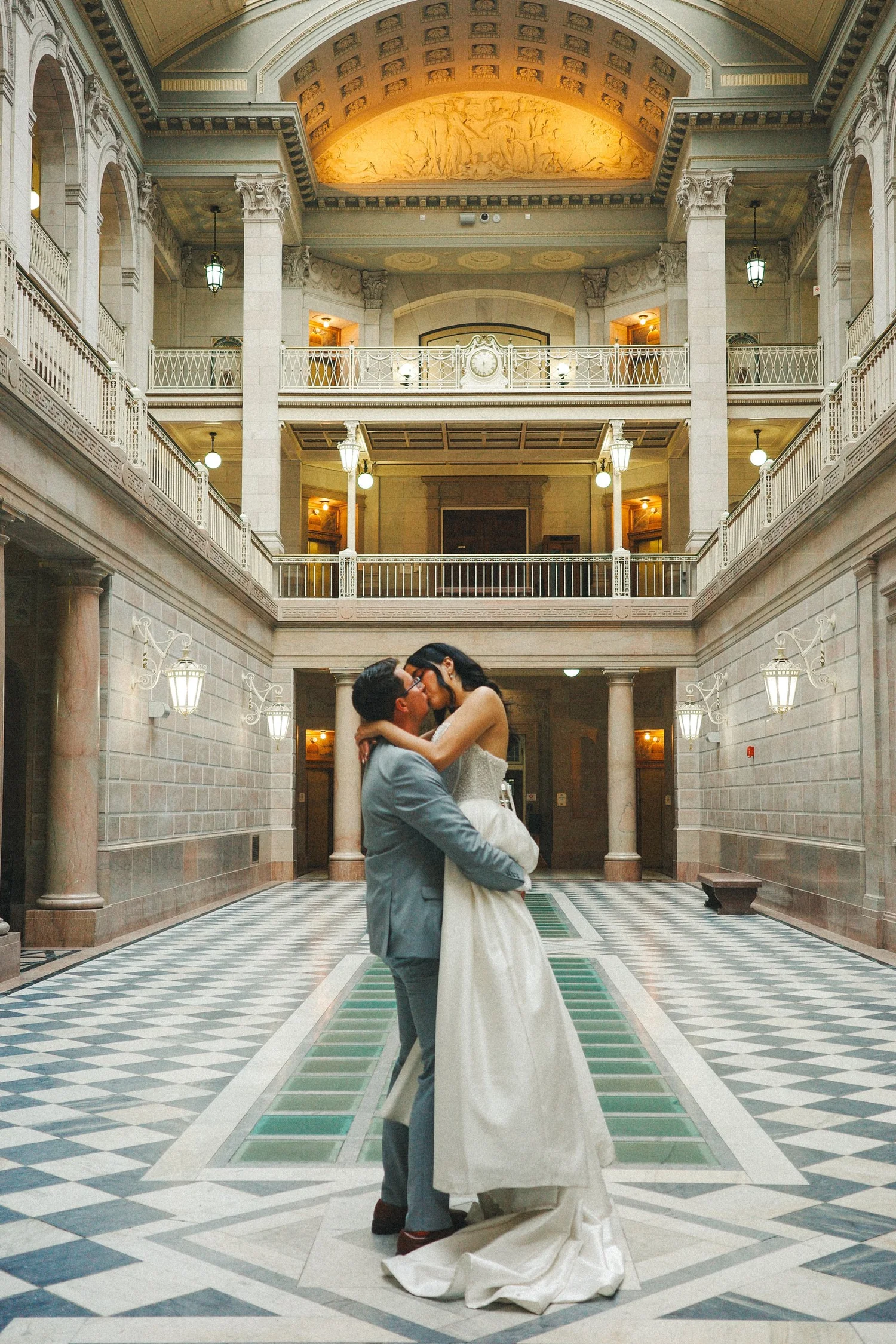 Bride and groom kissing in the center of the Beaux-Arts marble atrium beneath the illuminated stained-glass skylight at Hartford City Hall in Hartford, CT