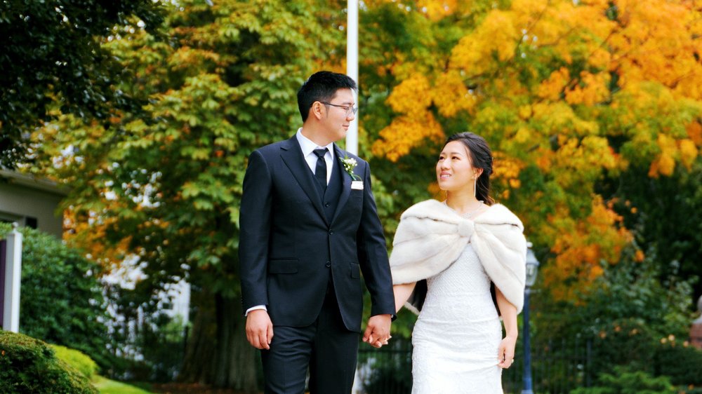 The Gardens at Elm Bank wedding videographer, Wellesley, MA — bride and groom walking hand in hand beneath golden autumn foliage