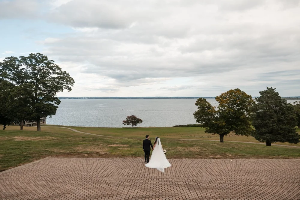 Aldrich Mansion wedding photographer, Warwick, RI — wide view of the bride and groom walking across the stone terrace toward the 70-acre Narragansett Bay lawn