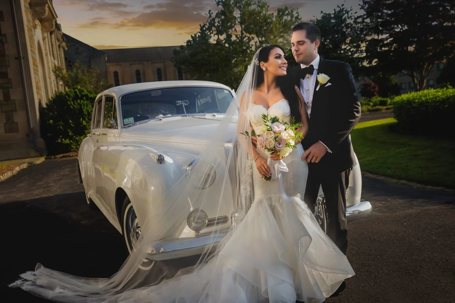 Aldrich Mansion wedding photographer, Warwick, RI — bride and groom beside a vintage white Rolls-Royce under a golden sunset sky