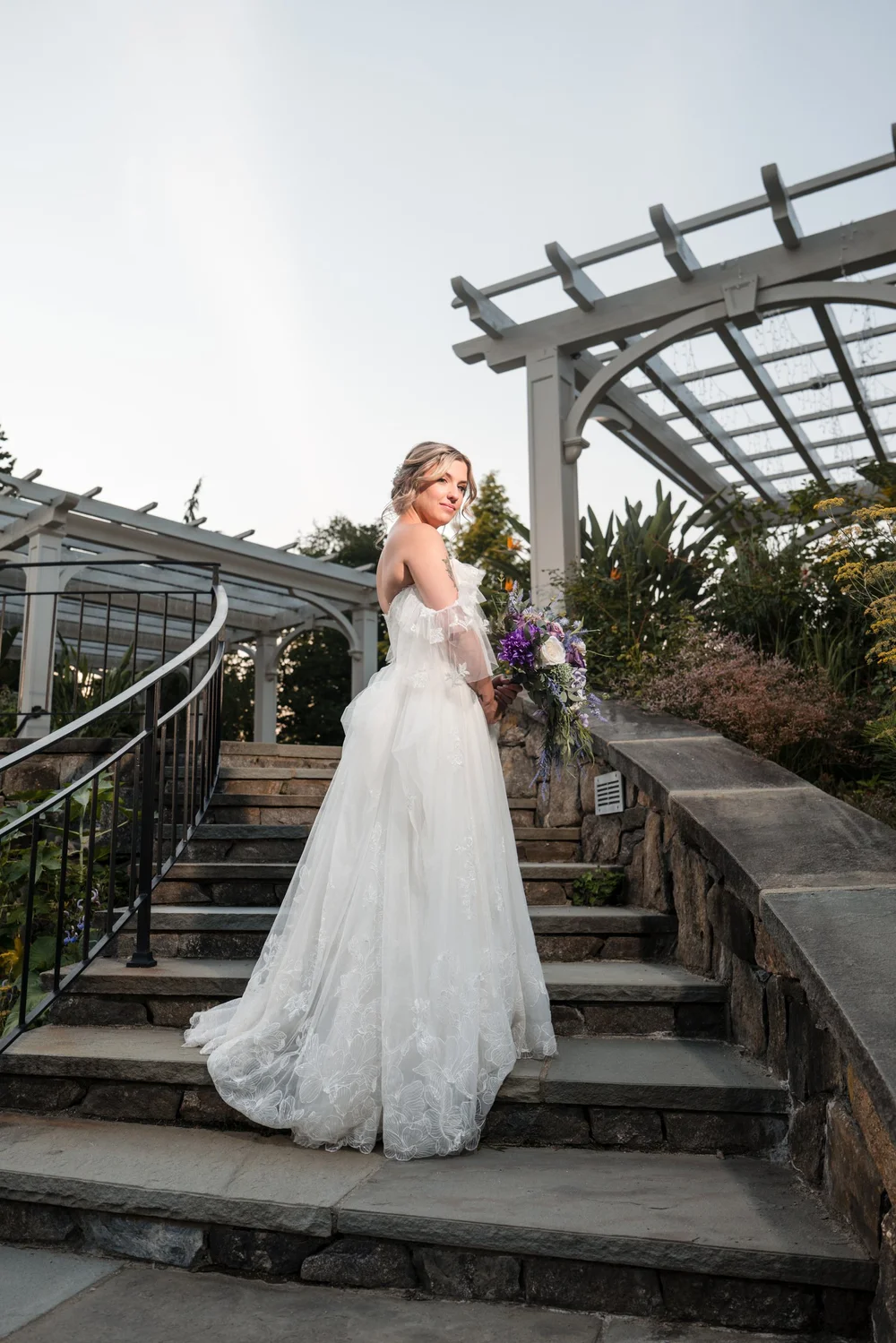 Fine-art monochrome bridal portrait standing on the stone steps beside the garden pergola columns at New England Botanic Garden at Tower Hill, Boylston, MA