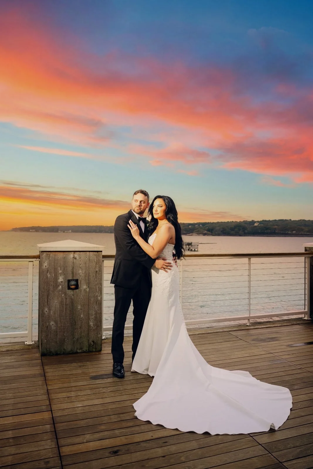 Beauport Hotel wedding videographer, Gloucester, MA — bride and groom on the harborfront deck beneath a vivid pink and orange sunset