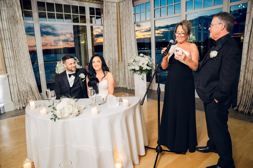 Beauport Hotel wedding photographer, Gloucester, MA — toasts at the sweetheart table in front of floor-to-ceiling windows as the sun sets over Gloucester Harbor