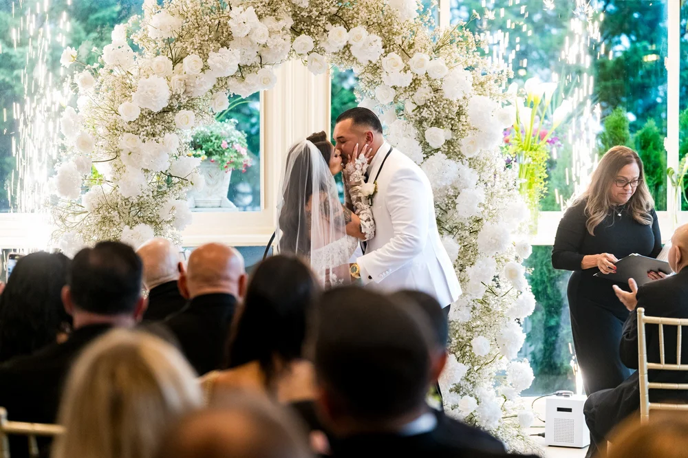 Anthony's Ocean View wedding photographer, New Haven, CT — first kiss under a white rose and baby's breath floral arch