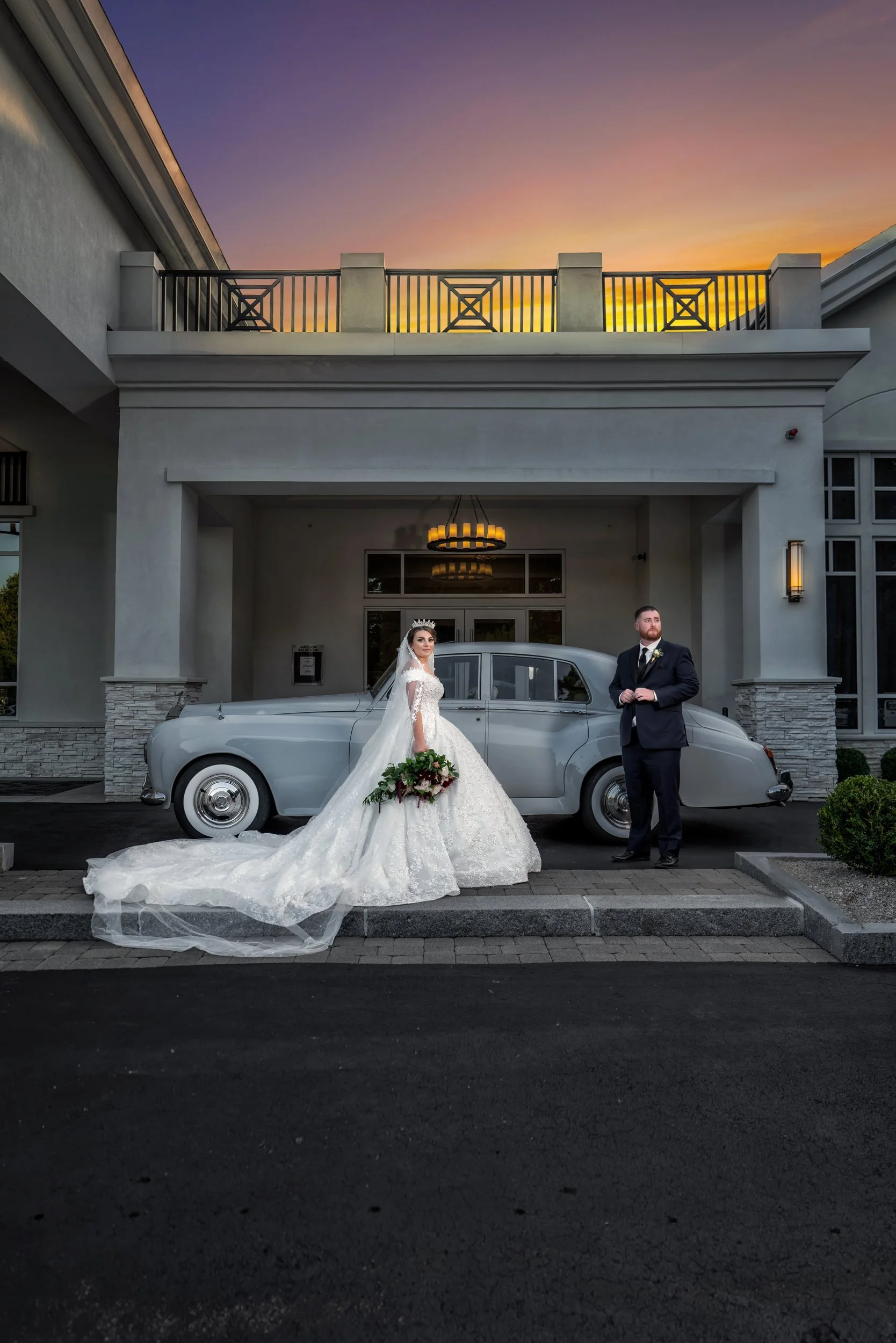 Couple beside a vintage car at the Lakeview Pavilion entrance at sunset, Foxborough, Massachusetts