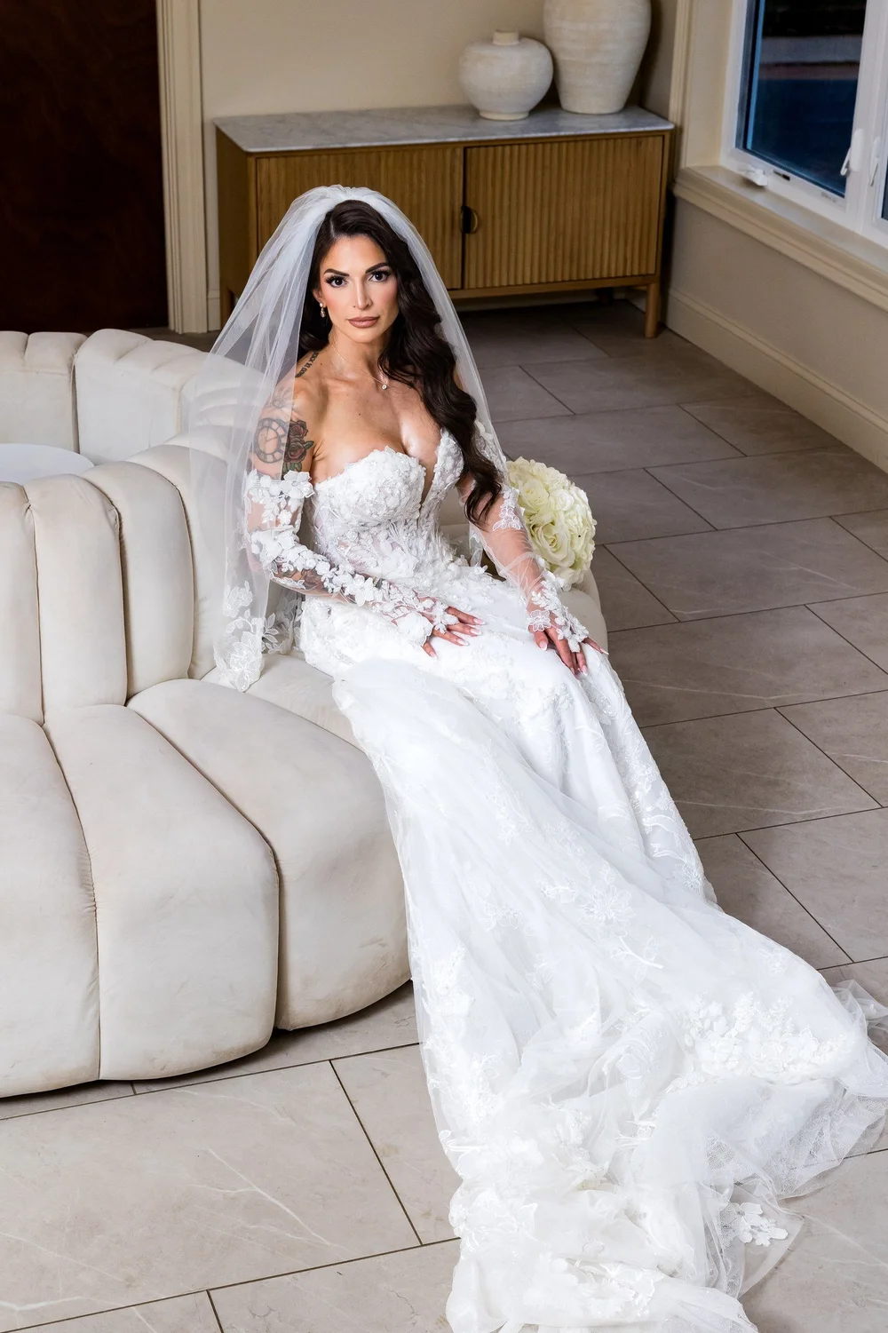 Anthony's Ocean View wedding photographer, New Haven, CT — bride seated on a curved velvet sofa in the bridal suite with her lace train