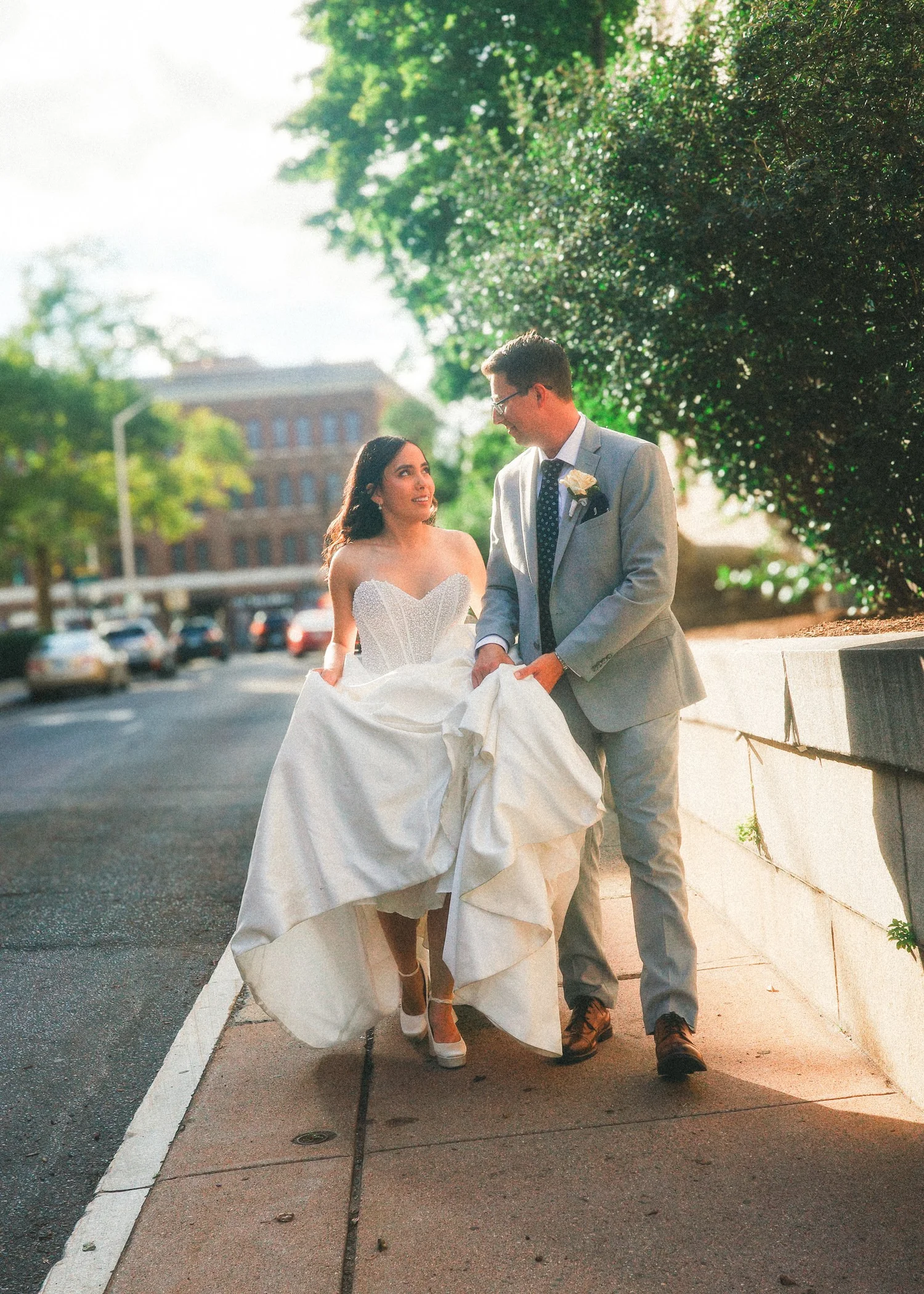 Sun-drenched outdoor wedding portrait of the bride and groom walking along the historic stone wall outside Hartford City Hall in downtown Hartford, CT