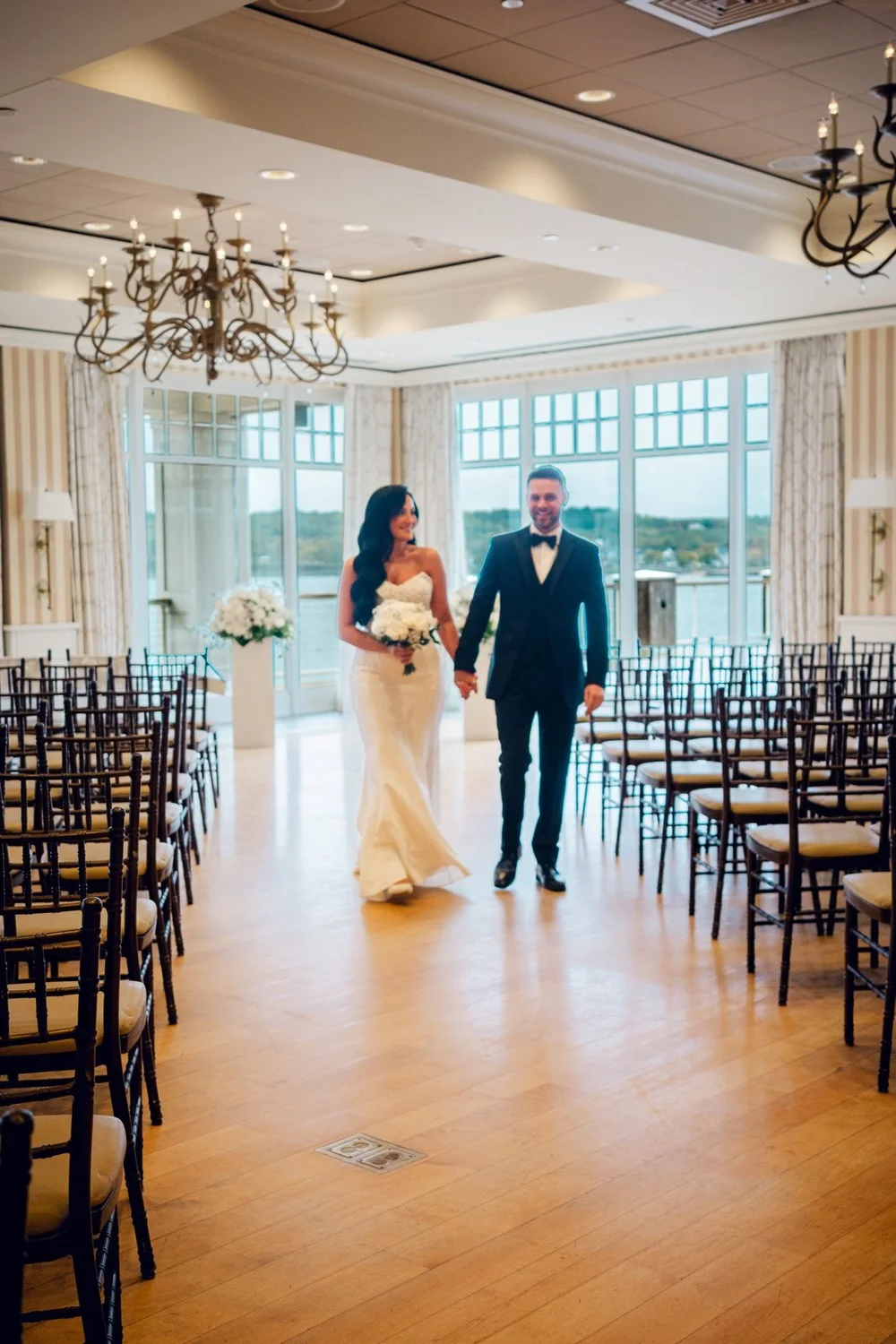 Beauport Hotel wedding videographer, Gloucester, MA — couple at the end of the aisle with harbor-view windows behind the ceremony seating