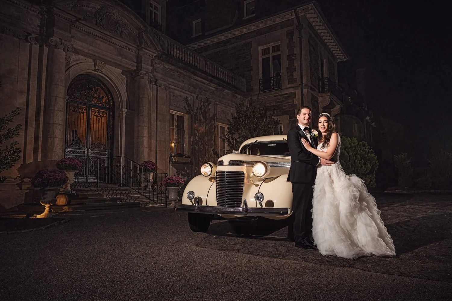 Aldrich Mansion wedding videographer, Warwick, RI — night portrait of the bride and groom beside a vintage cream classic car at the chateau entrance