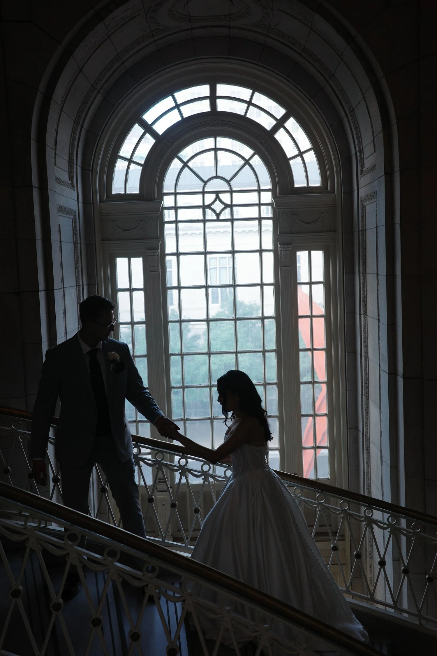 Dramatic silhouette of the bride and groom holding hands on the grand marble staircase in front of the arched Palladian window at Hartford City Hall, Hartford, CT