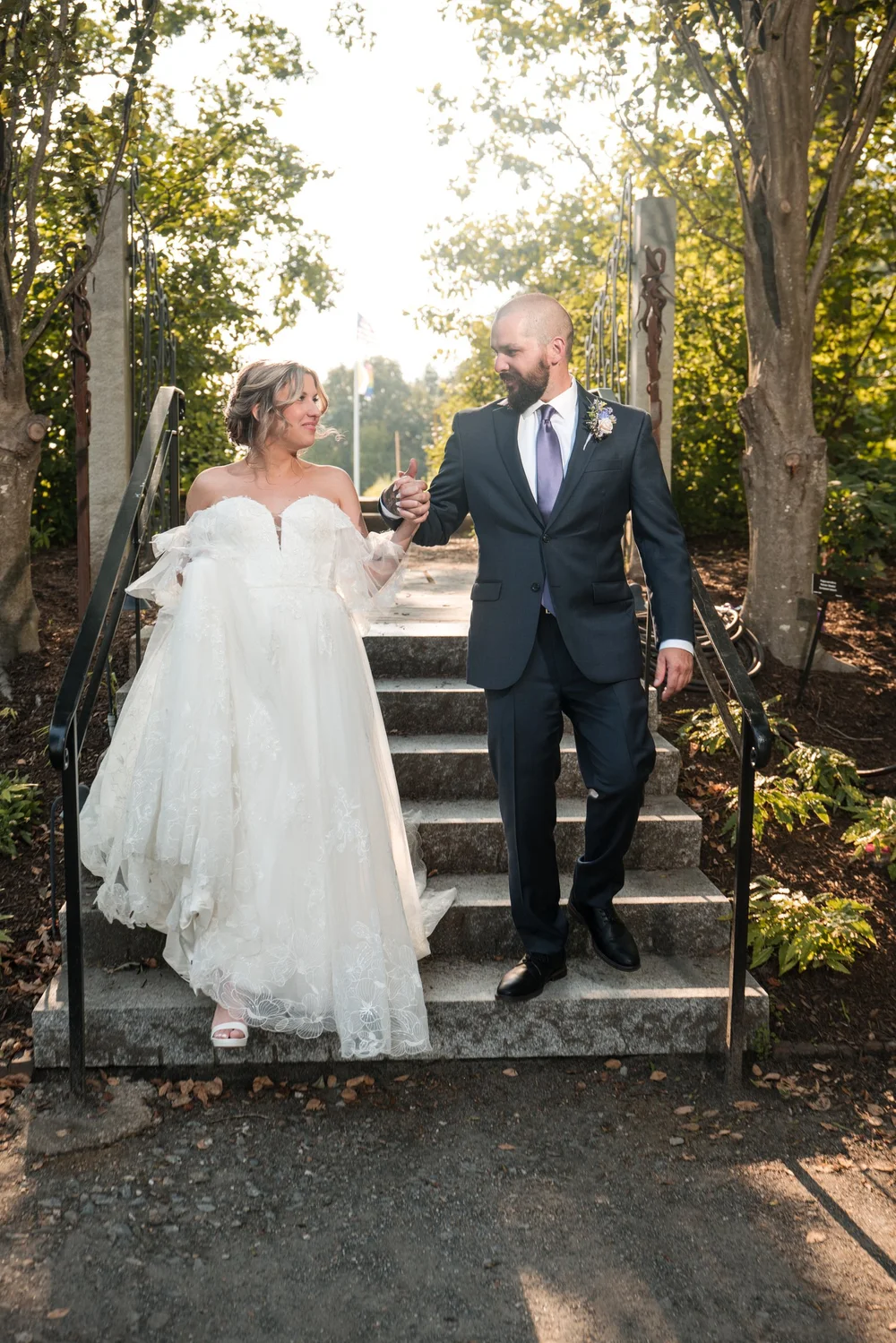 Bride and groom walking hand-in-hand down the outdoor stone garden stairs framed by lush summer greenery at New England Botanic Garden at Tower Hill, Boylston, MA