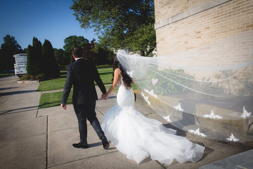 Aldrich Mansion wedding photographer, Warwick, RI — bride and groom walking hand in hand as her lace-trimmed veil catches the breeze