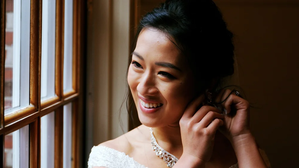 The Gardens at Elm Bank wedding photographer, Wellesley, MA — bride putting on her earring by the natural window light