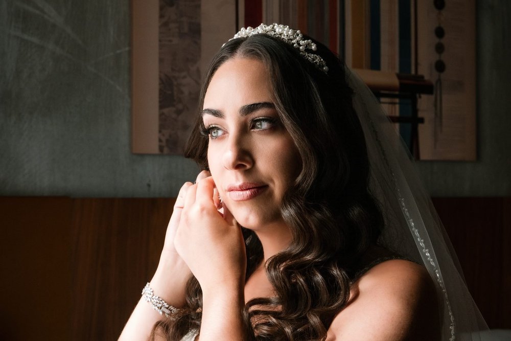 Aldrich Mansion wedding photographer, Warwick, RI — window-lit bridal portrait as the bride puts on her earrings and pearl tiara