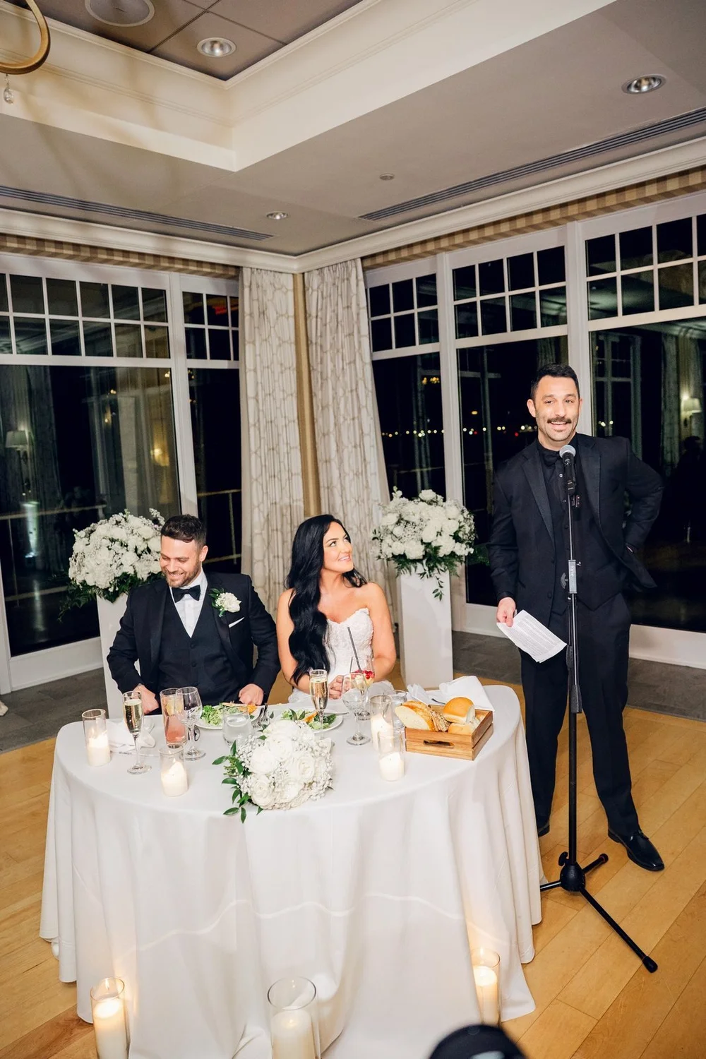 Beauport Hotel wedding photographer, Gloucester, MA — sweetheart table toast in front of the floor-to-ceiling harbor windows