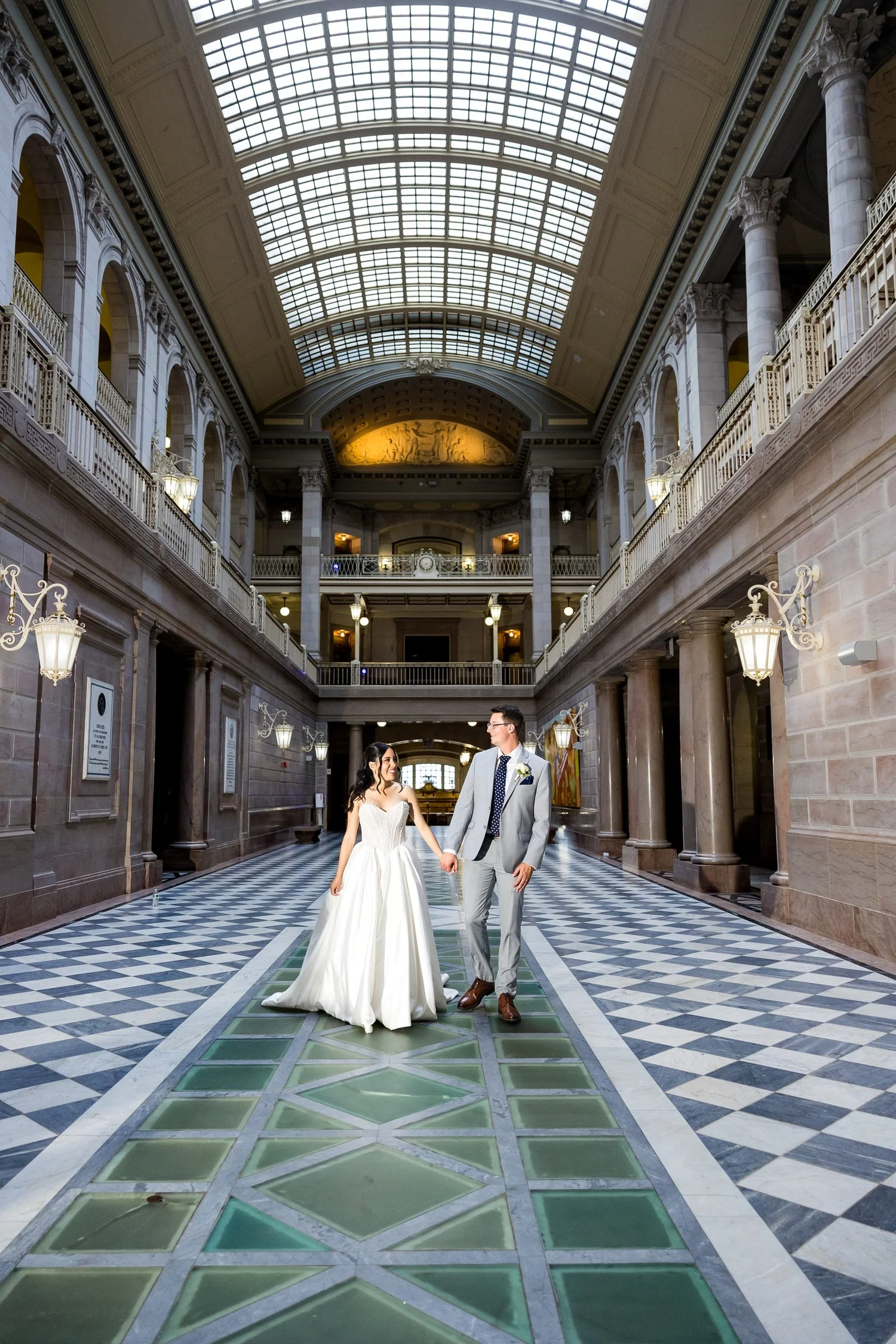 Bride and groom walking hand-in-hand down the black-and-white checkered marble floor flanked by neoclassical columns at Hartford City Hall in Hartford, CT