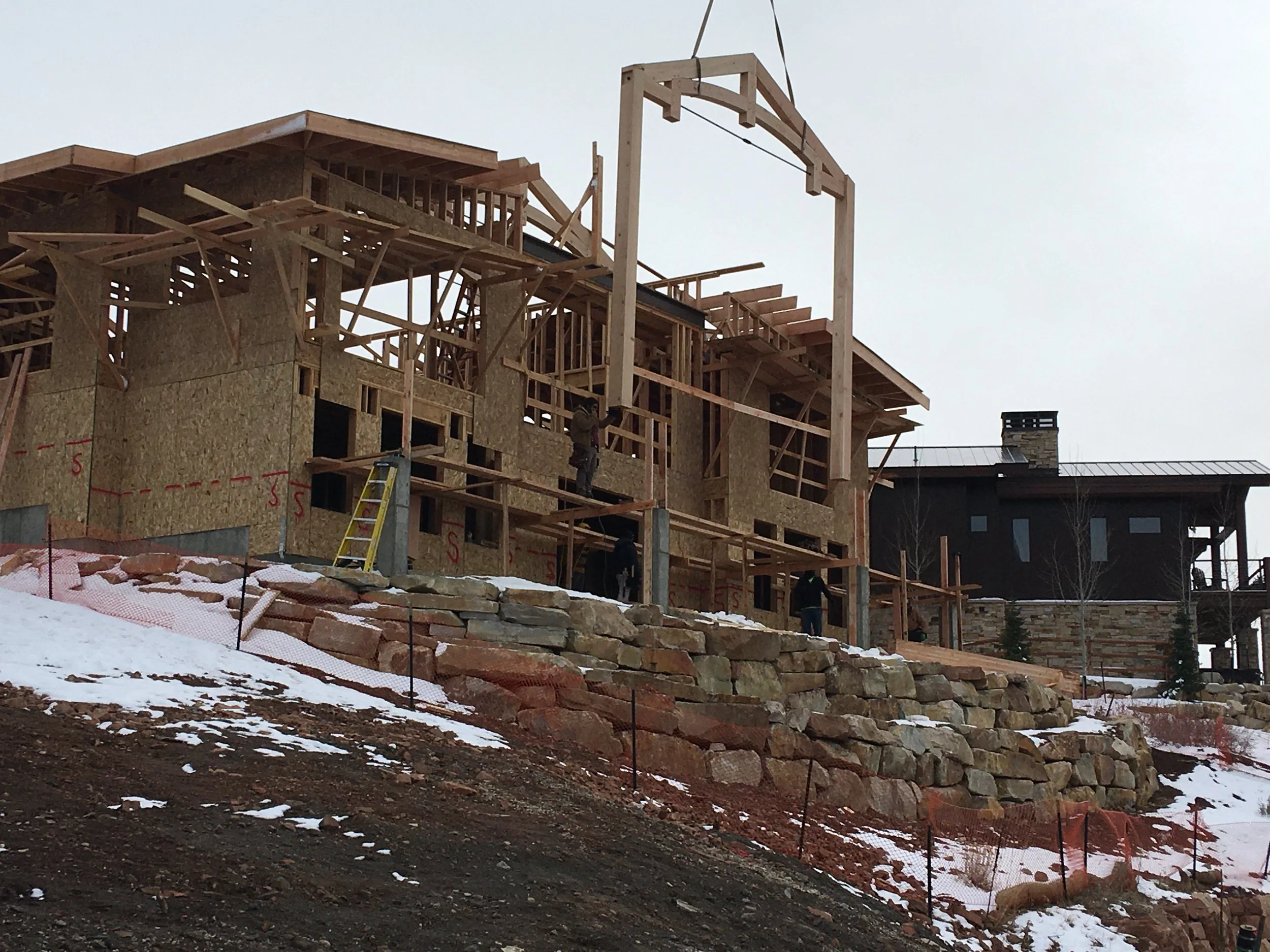 Crane setting a structural timber frame bent during home framing
