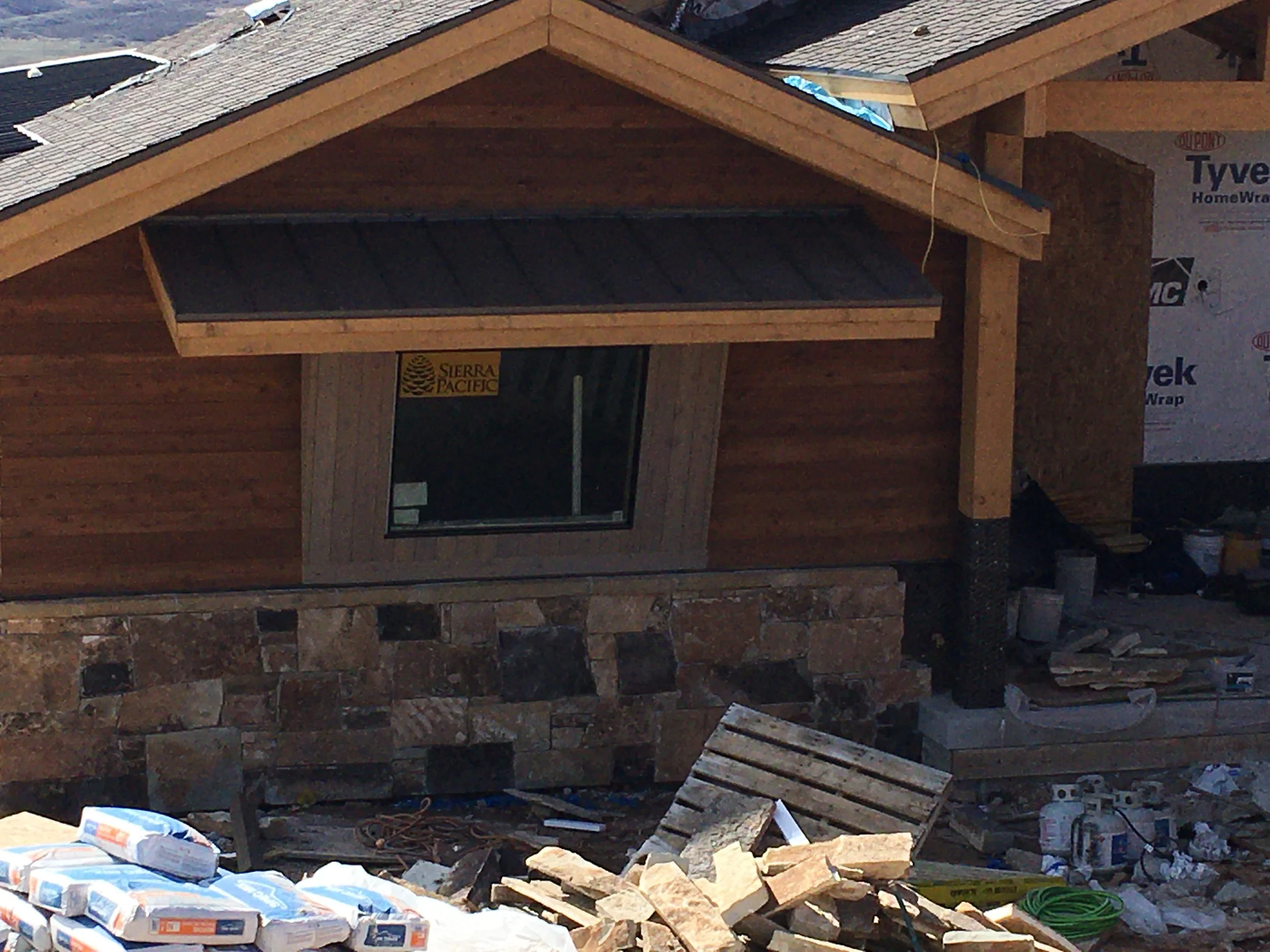 Home exterior under construction with wood siding, stone, and metal awning