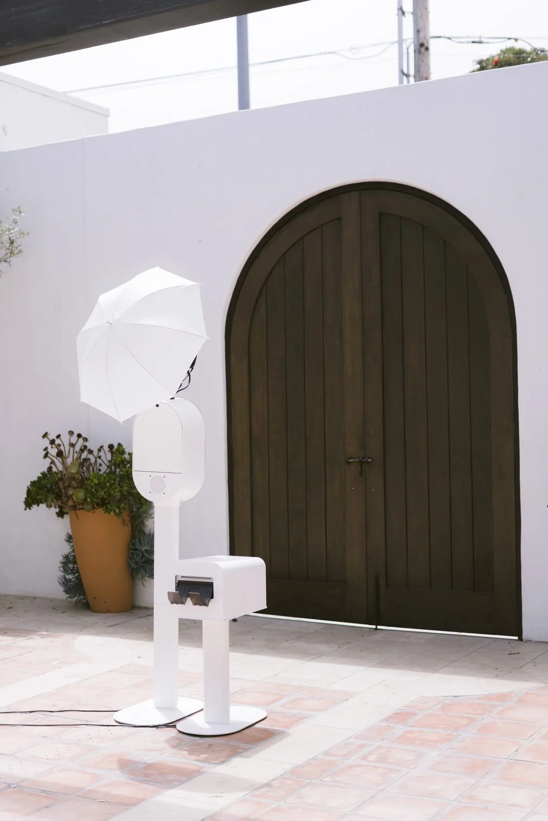 Wuddabooth photo booth set up beneath an arched wooden door in a sunlit courtyard