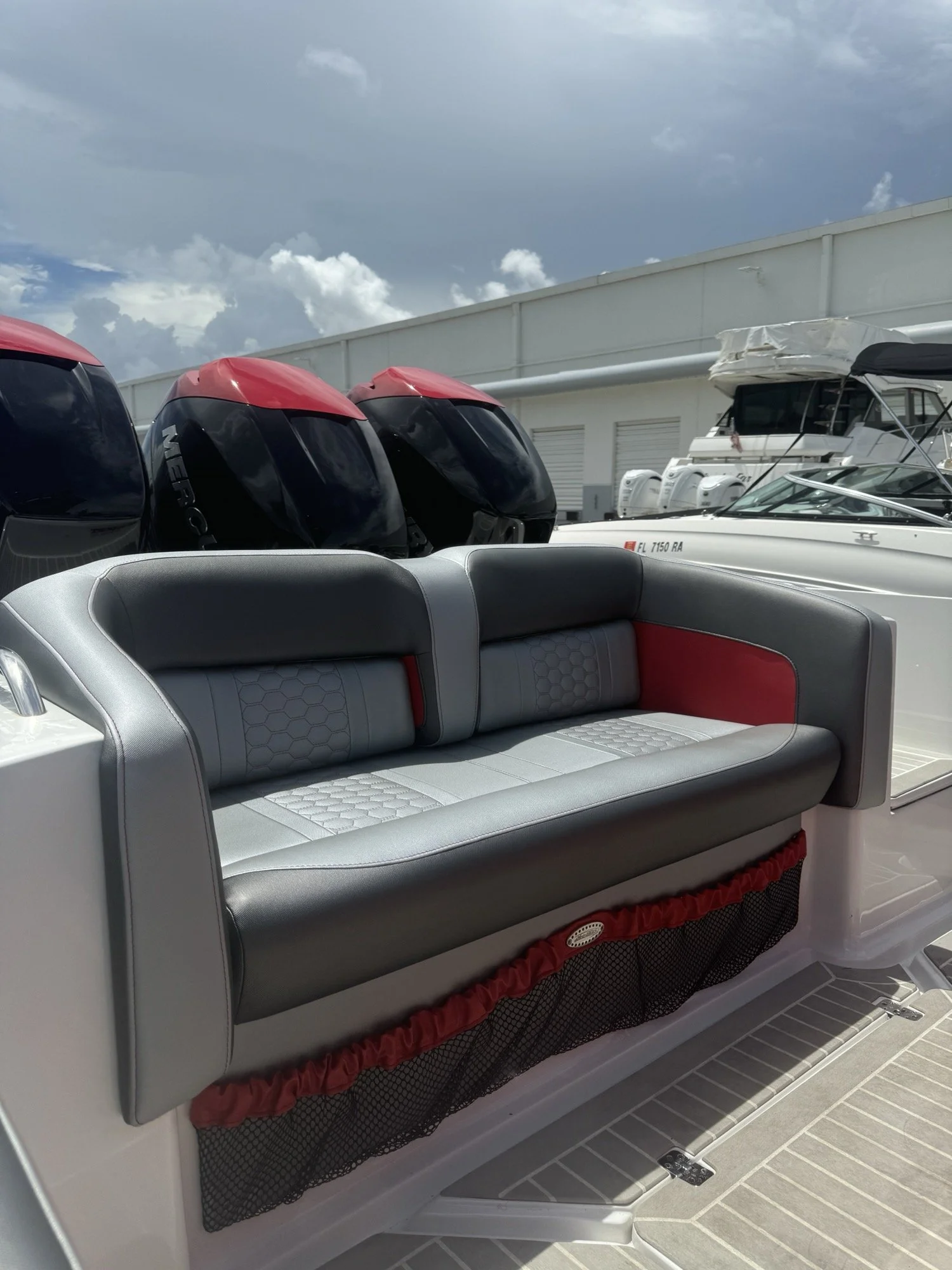 Grey and red aft bench seating with hexagon quilting and a red-trimmed netted storage pocket, on a triple-outboard center console