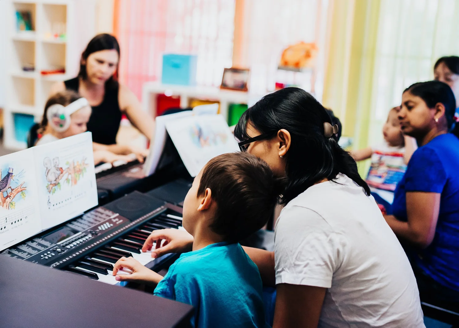 A child leaning close to his mother while they learn together at the piano