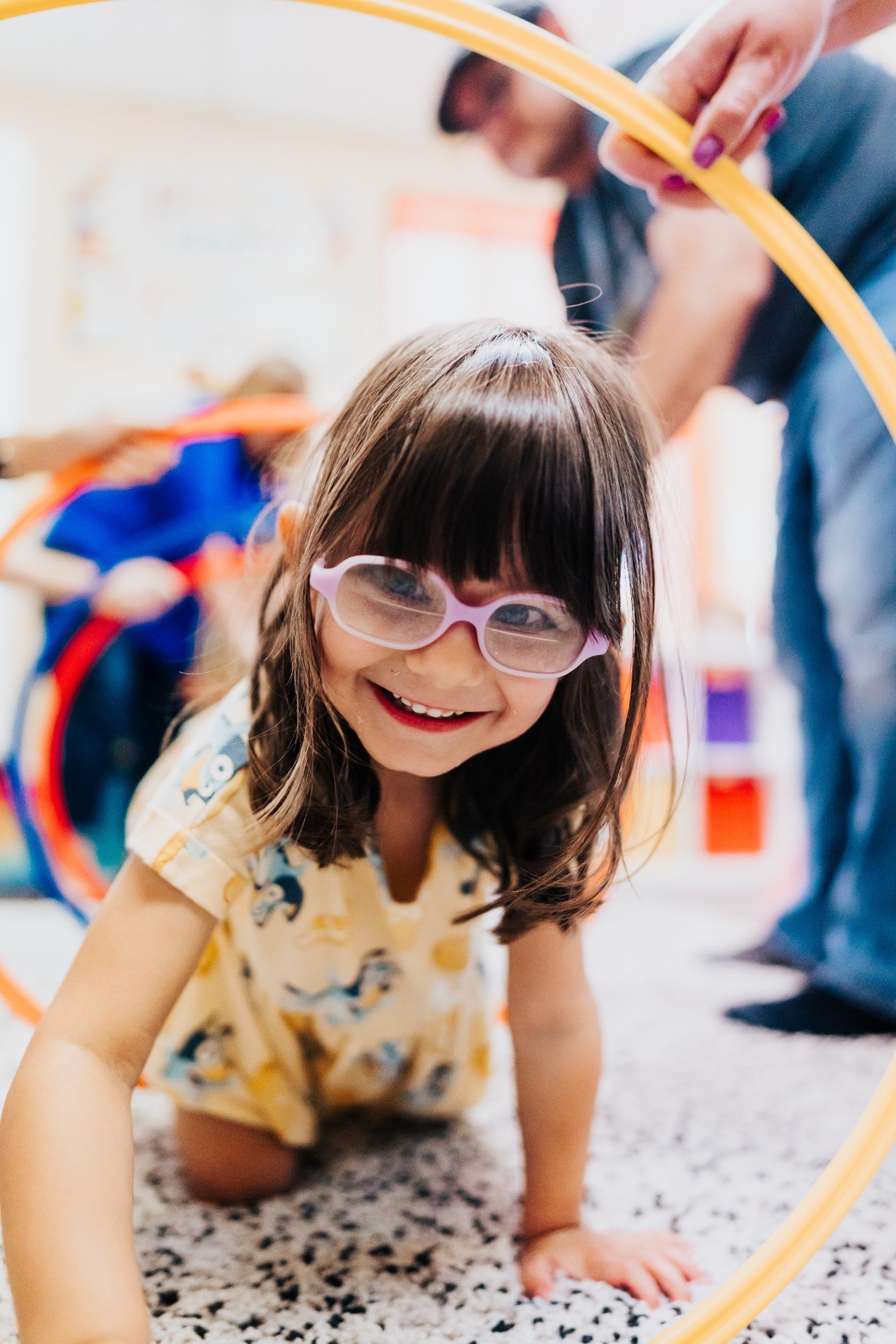 A smiling child in purple glasses discovering music through joyful movement and rainbow hoops