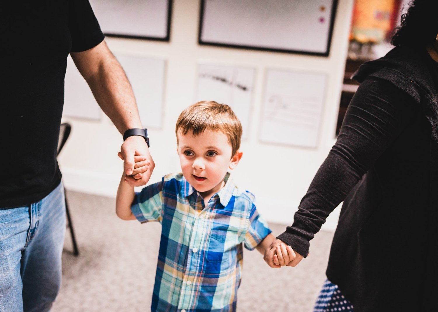 A child smiling while holding his parents’ hands and moving to music