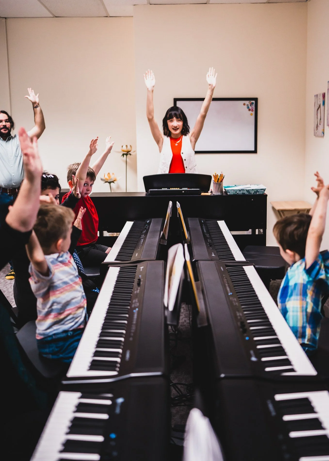 Children and their grown-ups raising their hands together at the keyboards
