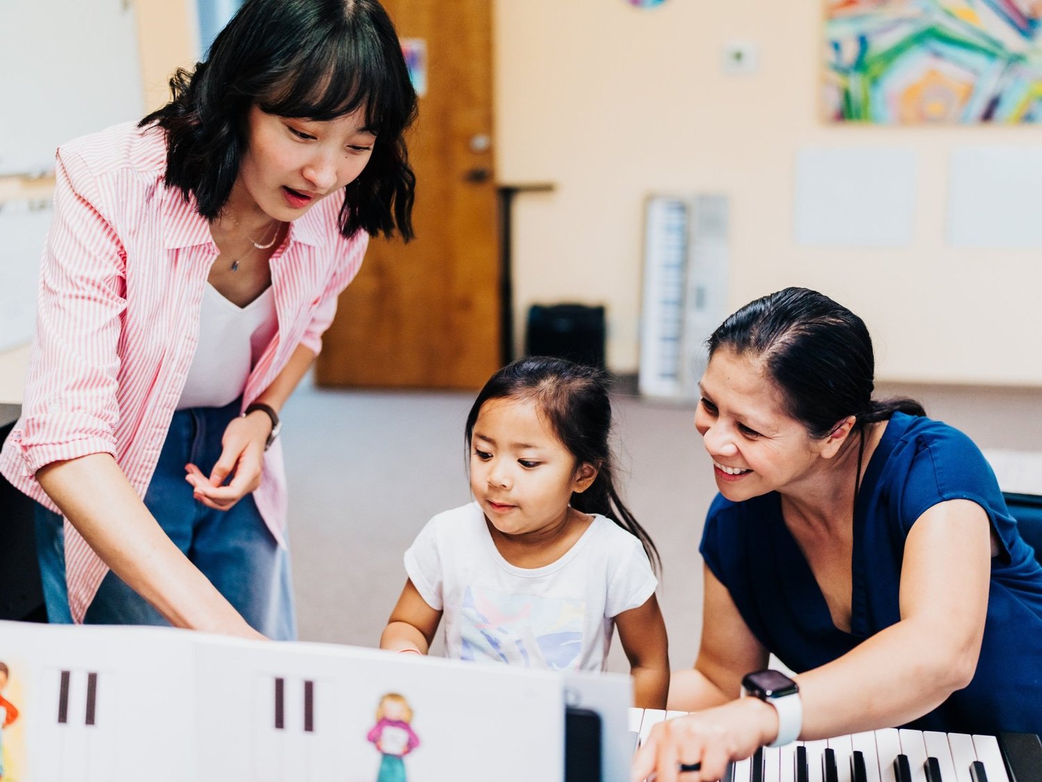 Annie leaning over a keyboard to teach a child and her mother together