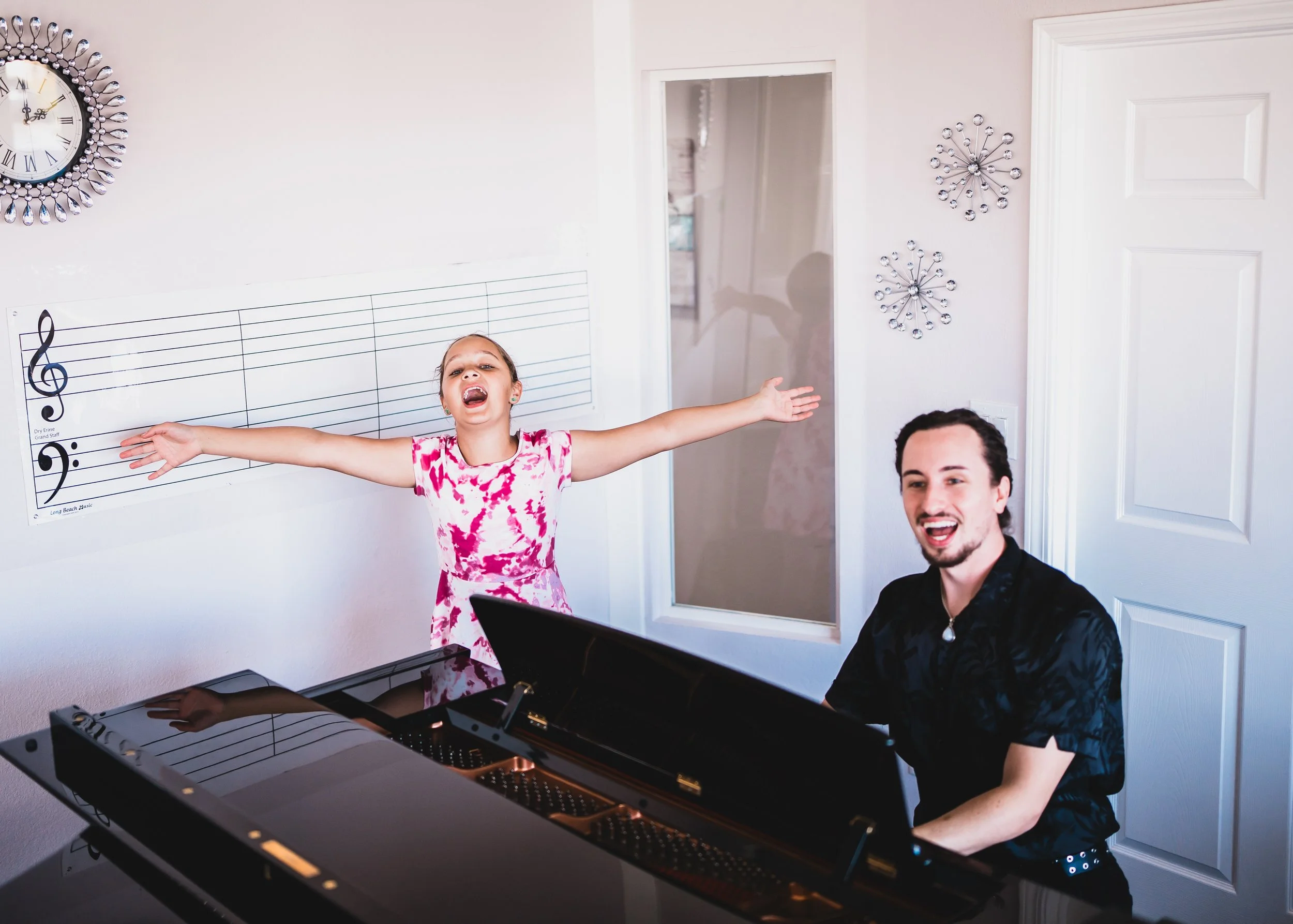 A Heart Beats student in a pink floral dress singing with her arms open while her teacher sings alongside her