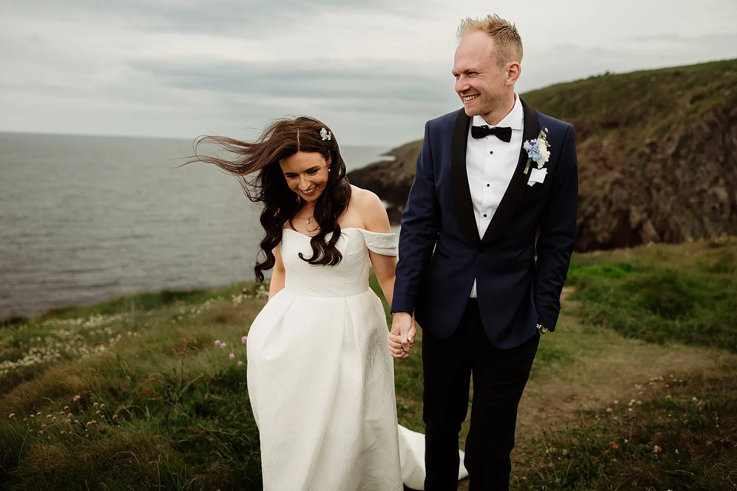 Aoife laughing as the wind catches her hair, walking hand in hand with Dan on the East Cork clifftops