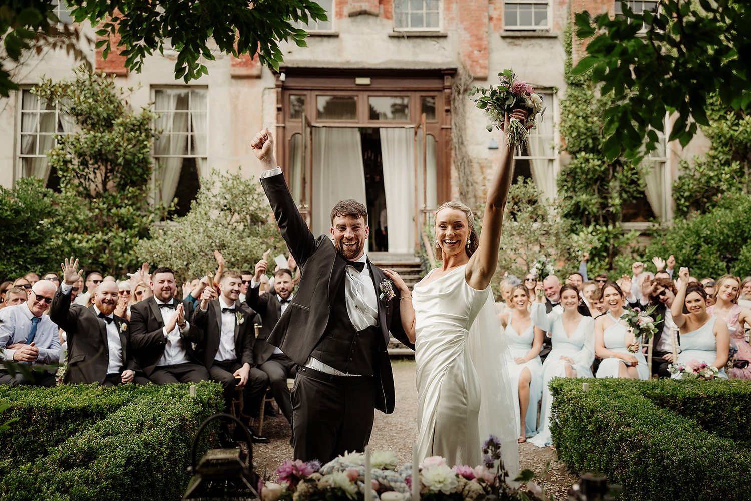Ellen and Aaron with their arms in the air as their guests cheer after the ceremony