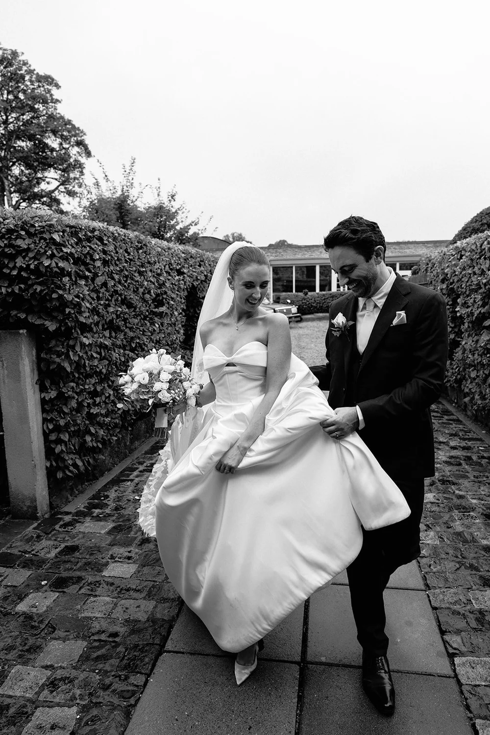 Megan and Rob laughing as they walk together, with Rob helping to carry her wedding dress
