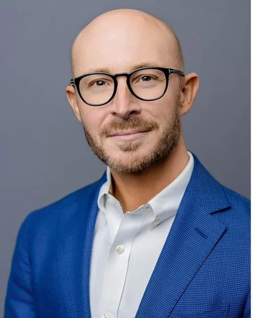 Conference headshot by Jack Robert Photo: smiling man in a blue blazer and glasses on a grey backdrop