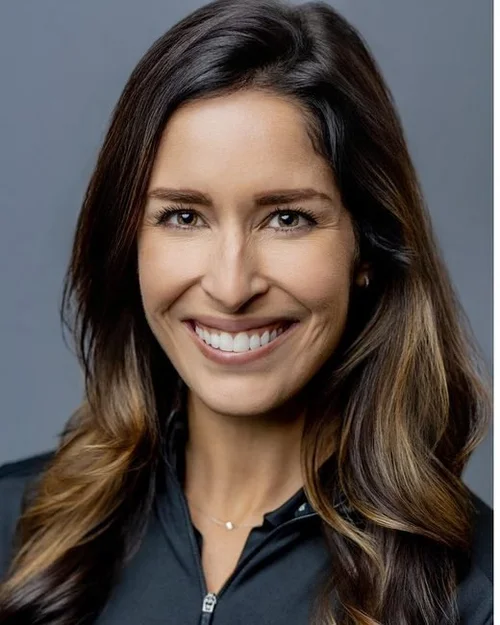 Conference headshot: smiling woman with long brown hair on a grey backdrop