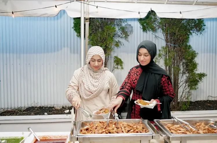 Two guests serving themselves grilled skewers from the buffet at the outdoor reception