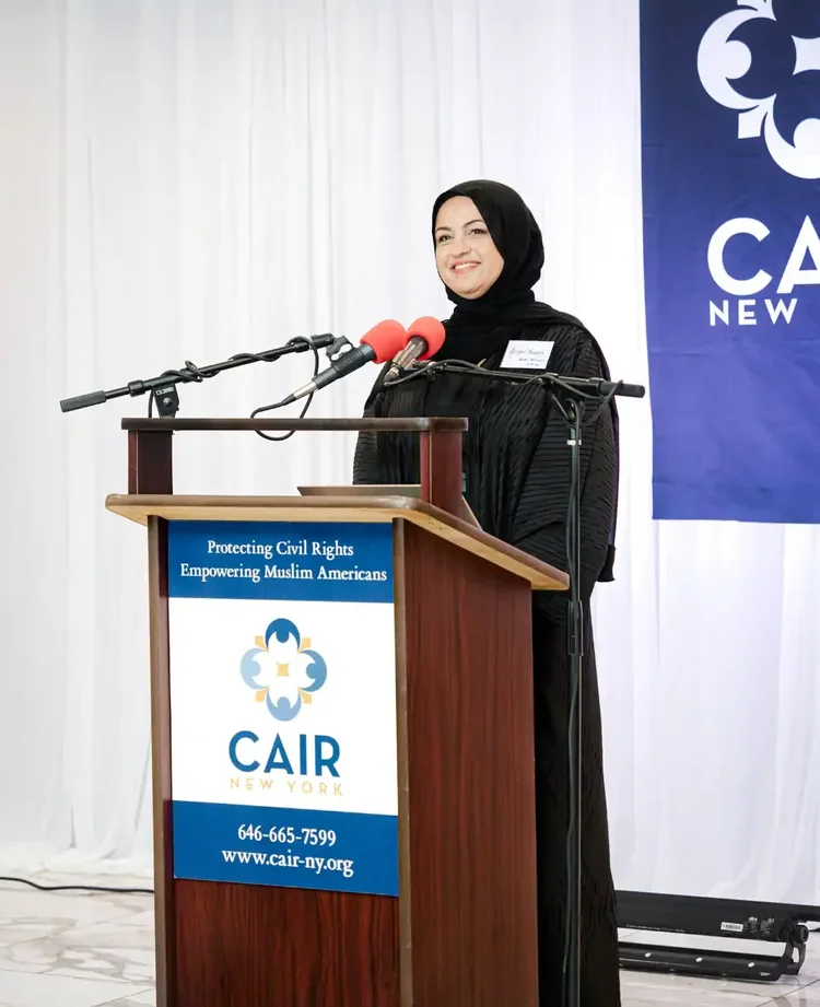 A CAIR-NY staff member speaking from the podium in front of the CAIR New York banner